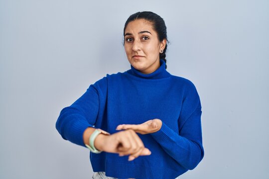 Young hispanic woman standing over isolated background in hurry pointing to watch time, impatience, upset and angry for deadline delay