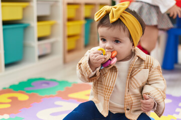 Adorable blonde toddler sitting on floor sucking toy at kindergarten