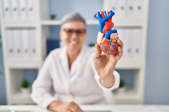 Middle age woman wearing doctor uniform holding heart at clinic