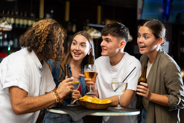Group of happy carefree people spending time in pub, drinking beer with snacks and chatting in friendly way