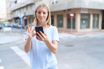 Fototapeta na wymiar Young blonde woman smiling confident using smartphone at street