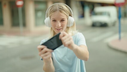 Young blonde woman smiling confident playing video game at street