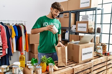 Young arab man wearing volunteer uniform insert food on paper bag at charity center