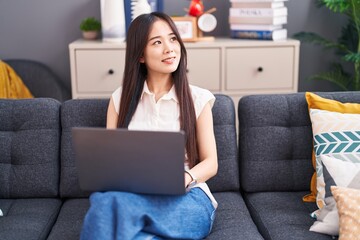 Young chinese woman using laptop sitting on sofa at home