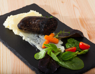 Fried morcilla (blood sausage with rice) served on white plate with pureed potatoes, vegetables and...
