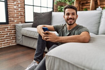 Young hispanic man smiling confident using smartphone at home