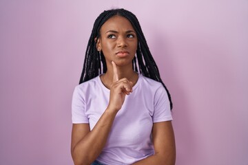 African american woman with braids standing over pink background thinking concentrated about doubt with finger on chin and looking up wondering