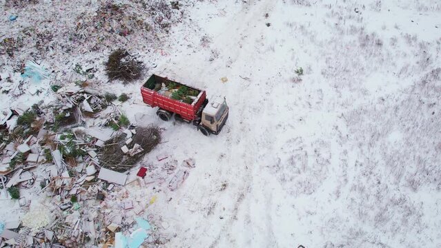 Top view of a dump truck unloading garbage at a vast landfill outside the city on a winter day. The concept of waste disposal
