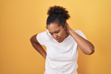 Fototapeta na wymiar Young hispanic woman with curly hair standing over yellow background suffering of neck ache injury, touching neck with hand, muscular pain