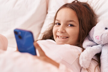 Obraz na płótnie Canvas Adorable hispanic girl using smartphone lying on bed at bedroom