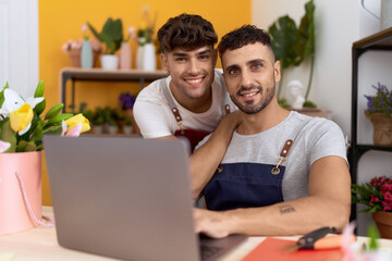Obraz premium Two hispanic men florists smiling confident using laptop working at flower shop