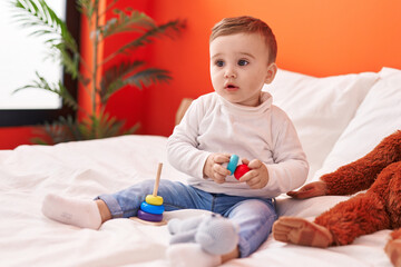 Naklejka premium Adorable caucasian baby playing with toys sitting on bed at bedroom