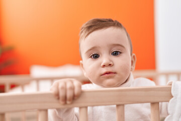 Adorable caucasian baby standing on cradle with relaxed expression at bedroom