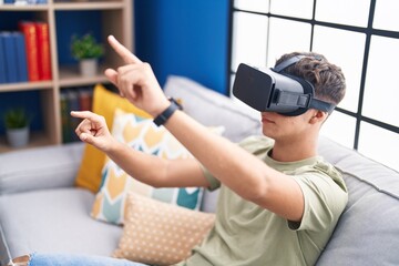 Young hispanic teenager playing video game using virtual reality glasses at home