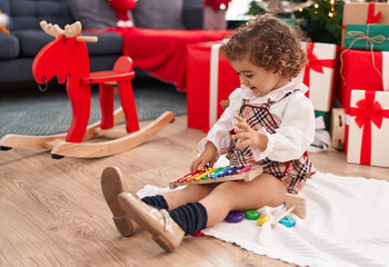 Adorable hispanic girl playing xylophone sitting on floor by christmas tree at home