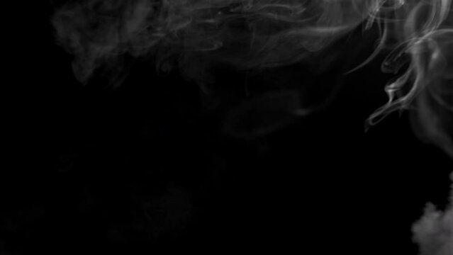 Abstract video of billowing smoke from a fire. How clouds float and form. Strong puffs of smoke on a black background. High quality 4k footage