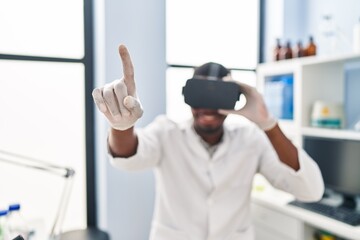 Naklejka na ściany i meble Young african american man wearing scientist uniform using virtual reality glasses at laboratory