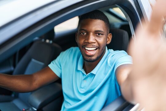 Young african american man making selfie by the camera sitting on car at street