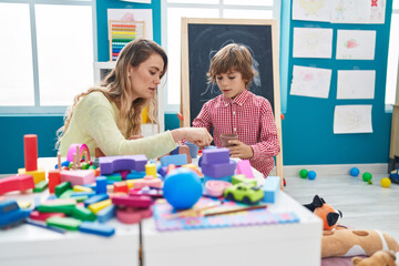 Naklejka premium Teacher and toddler playing with geometry blocks sitting on table at kindergarten