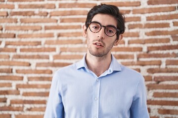 Obraz premium Young hispanic man standing over brick wall background looking sleepy and tired, exhausted for fatigue and hangover, lazy eyes in the morning.