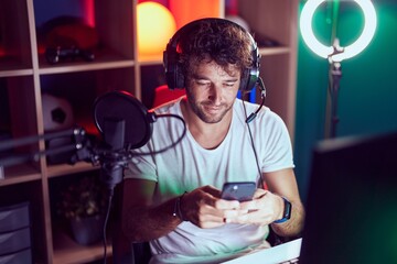 Young hispanic man streamer using computer and smartphone at music studio