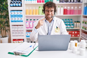 Hispanic young man working at pharmacy drugstore working with laptop smiling happy pointing with hand and finger