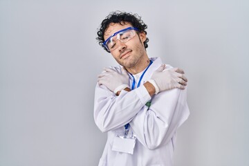 Hispanic man working at scientist laboratory hugging oneself happy and positive, smiling confident. self love and self care