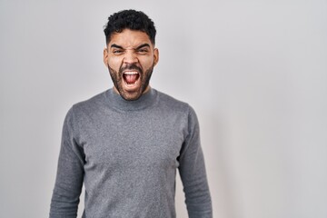 Hispanic man with beard standing over white background angry and mad screaming frustrated and furious, shouting with anger. rage and aggressive concept.