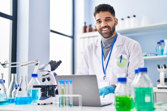 Young hispanic man wearing scientist uniform using laptop at laboratory