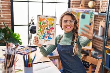 Young woman artist smiling confident making selfie by smartphone at art studio