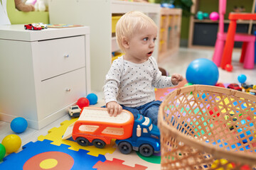 Adorable blond toddler playing with cars toy sitting on floor at kindergarten