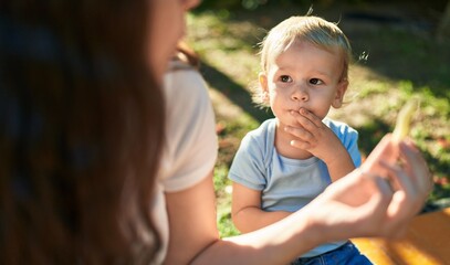 Fototapeta premium Mother and son sitting on bench together eating little worms snack at park