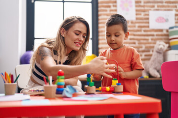 Teacher and toddler playing with toys sitting on table at kindergarten