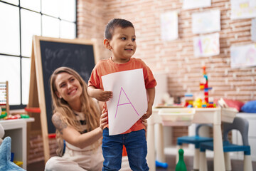 Teacher and toddler holding paper standing at kindergarten