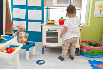 Adorable hispanic toddler playing with play kitchen standing at kindergarten