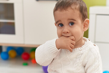 Adorable hispanic toddler sitting on floor sucking hand at kindergarten