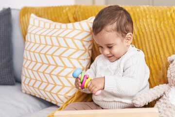 Adorable hispanic toddler playing with toy sitting on sofa at home