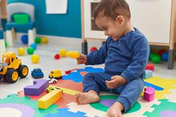 Naklejka premium Adorable hispanic toddler playing with construction blocks and bubbles at kindergarten