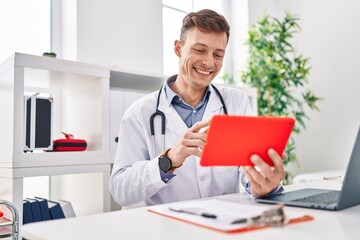 Fototapeta premium Young man doctor using touchpad sitting on table at clinic
