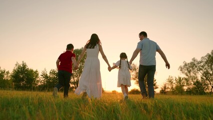 Happy family holding hands running towards sun and having fun in city park at sunset. Slow motion. Family, mom, dad daughter run together, happy childhood, freedom people, future, family game concept - Powered by Adobe