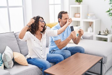 Man and woman couple watching tv with winner expression at home