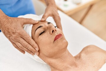 Middle age man and woman wearing therapist uniform having facial massage session at beauty center
