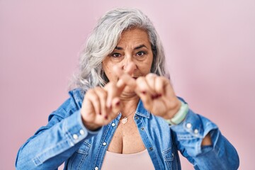 Middle age woman with grey hair standing over pink background rejection expression crossing fingers doing negative sign