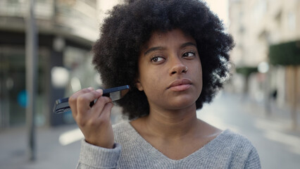 African american woman listening audio message by the smartphone with relaxed expression at street