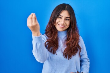 Hispanic young woman standing over blue background doing italian gesture with hand and fingers confident expression