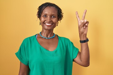 African woman with dreadlocks standing over yellow background showing and pointing up with fingers number two while smiling confident and happy.