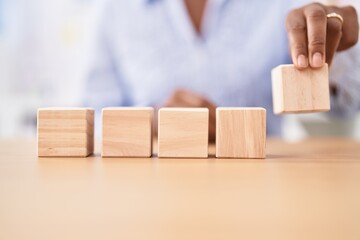 Middle age african american woman business worker sitting on table with wooden cubes at office