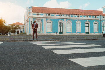A bald black man looking dapper in his Bordeaux custom-made suit standing in front of the zebrawalk...