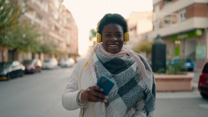 Young african american woman listening to music using smartphone at street