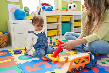 Fototapeta premium Teacher and toddler playing with hoops toys sitting on floor at kindergarten